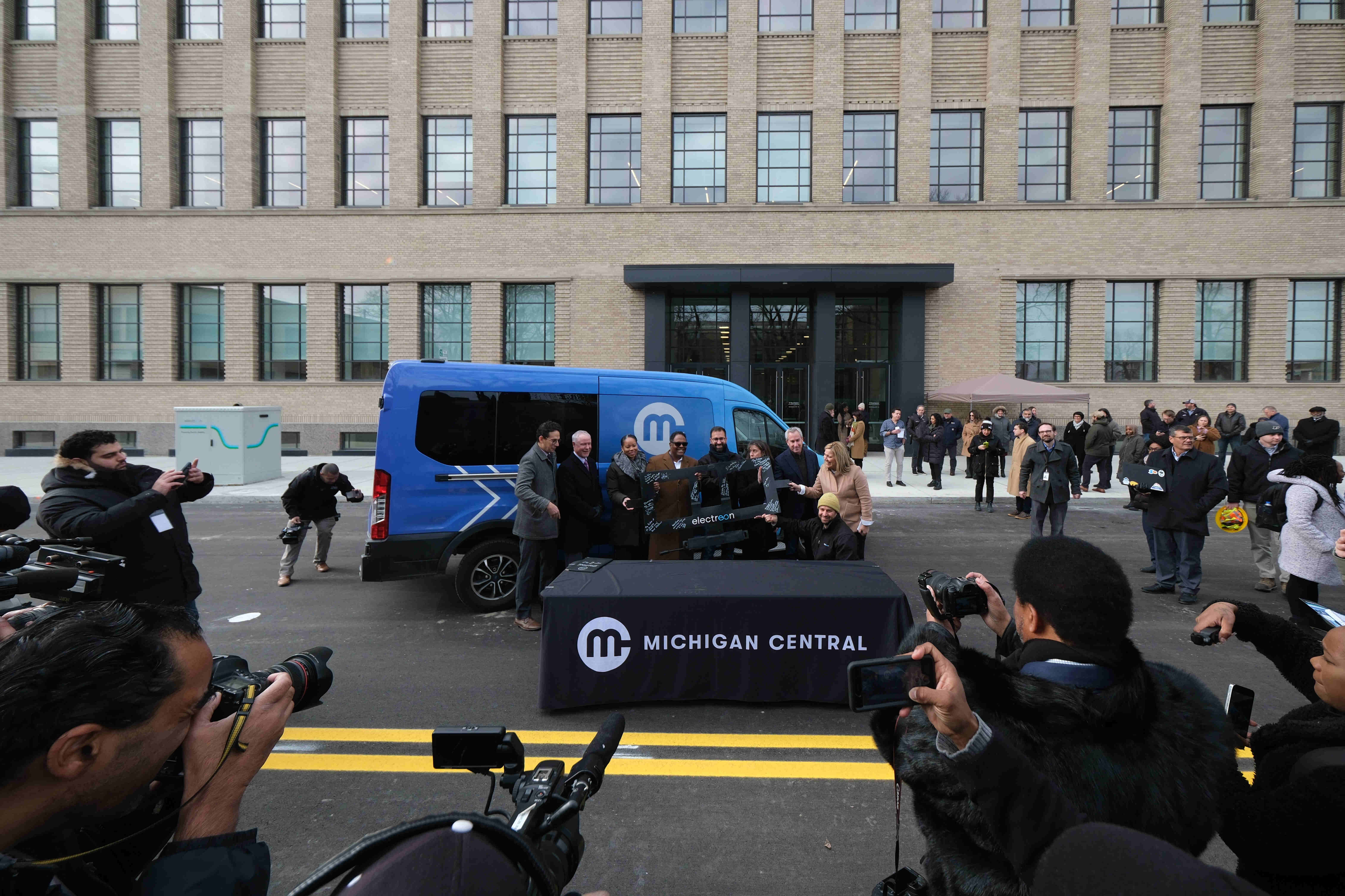 A press event around an blue van unveiling Electreon's first wireless charging road in Michigan. 