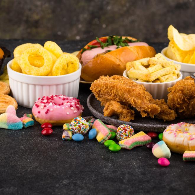An assortment of ultra-processed foods including donuts/pasties, candy, and fried foods such as potato chip, onion rings, fries, and breaded chicken.