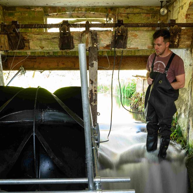 Senior Engineer Gregg Walker looks towards a "Picostream" floating turbine generator during installation in an old water mill.