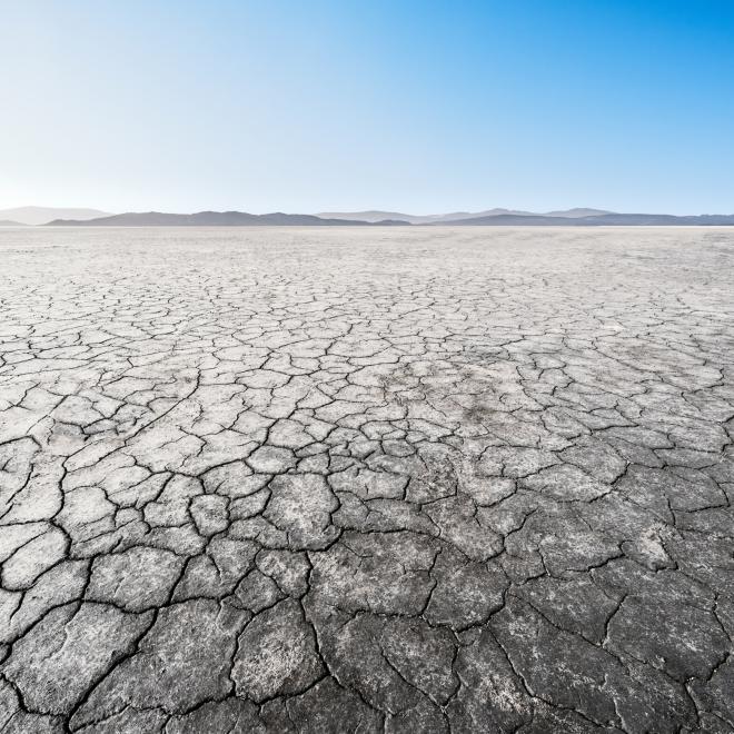 Arid, cracked, and desertified landscape against a blue sky. 