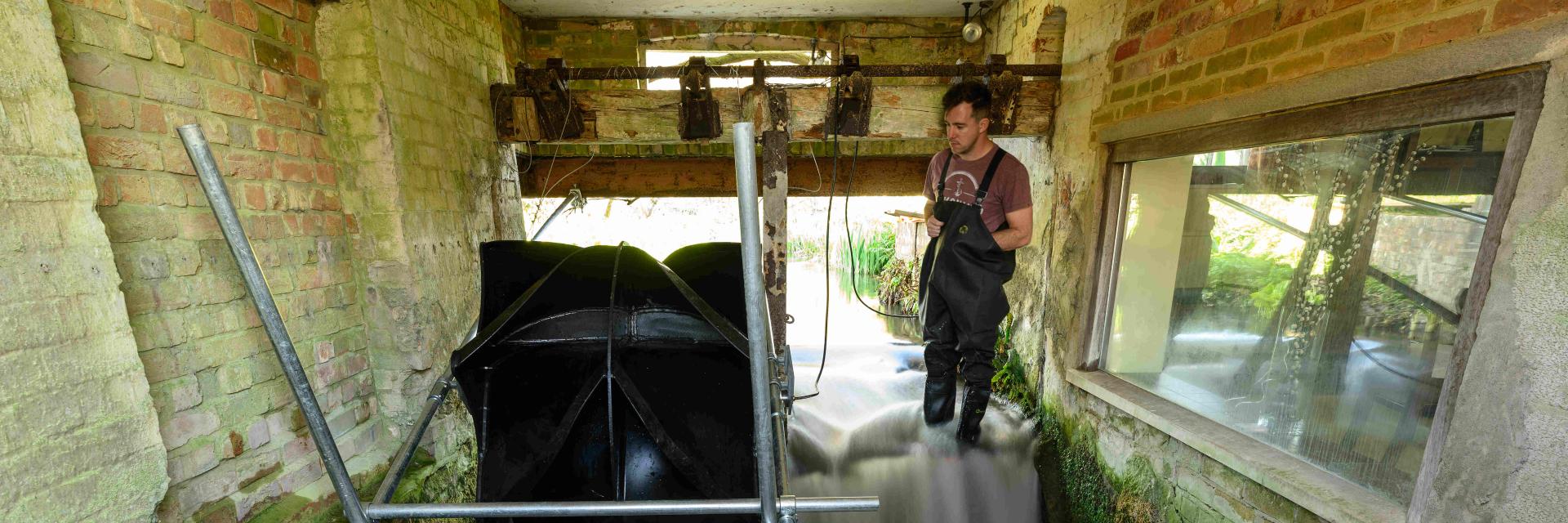 Senior Engineer Gregg Walker looks towards a "Picostream" floating turbine generator during installation in an old water mill.